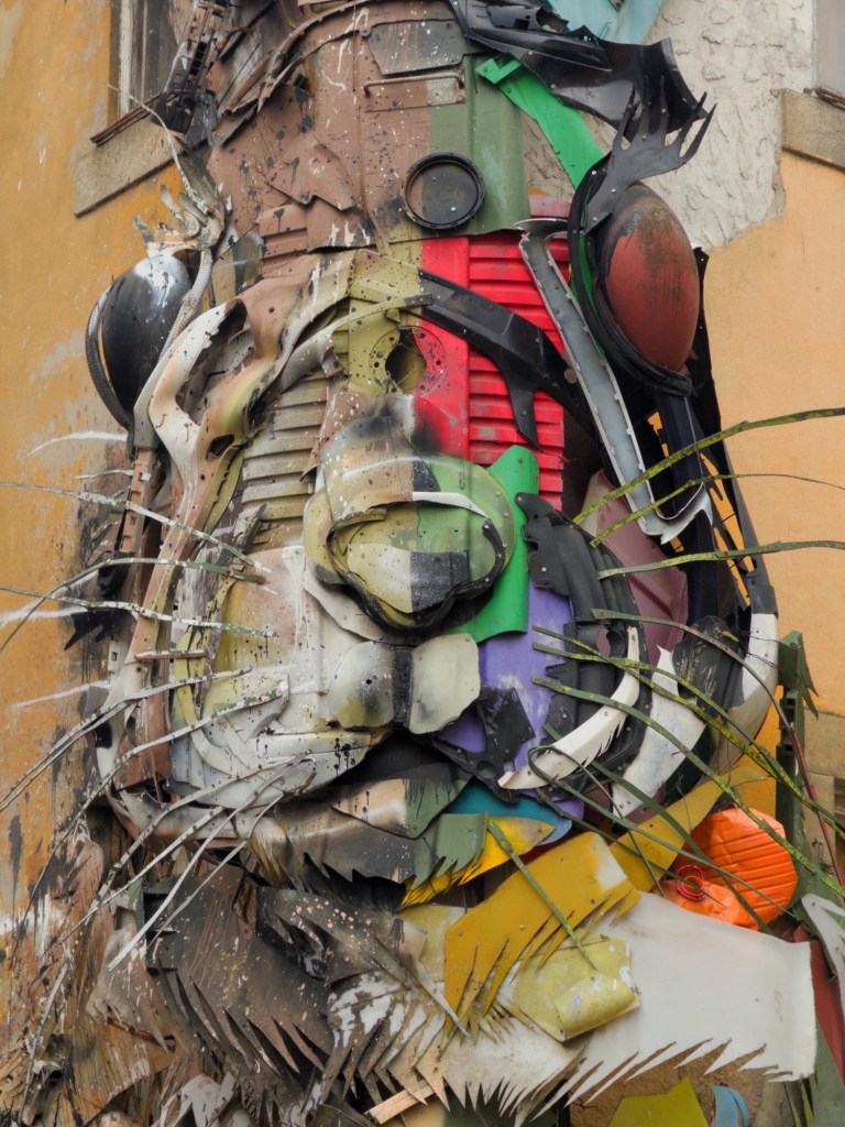 A large, colorful mural depicting a stylized animal face made from recycled materials, prominently featuring various shapes and textures.